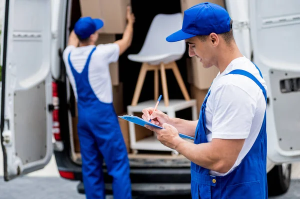 Twee verhuisbedrijf werknemers lossen dozen uit minibus in een nieuw huis — Stockfoto