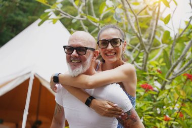 Bir erkek ve bir kadın büyük bir çadırın önünde sarılıp eğleniyorlar.