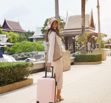 Bagajlı genç kadın yat limanının yanında yürüyor..