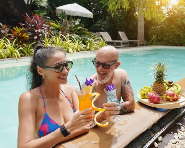 Bir erkek ve bir kadın havuzda dinlenirken kokteyllerin tadını çıkarırlar..