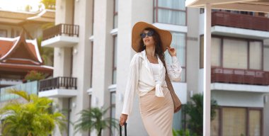 Bagajlı genç kadın yat limanının yanında yürüyor..