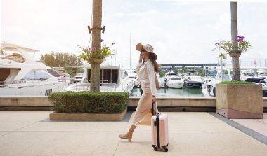 Bagajlı genç kadın yat limanının yanında yürüyor..