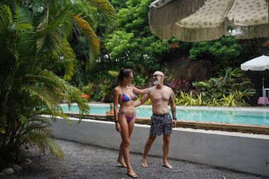 Bir adam ve bir kadın güzel bir havuzun önünde neşeyle yürüyorlar..