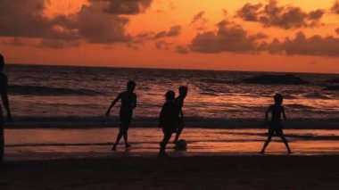 Gençler gün batımında okyanus kenarında futbol oynuyor..