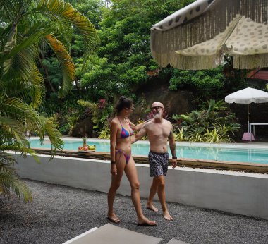 Bir adam ve bir kadın güzel bir havuzun önünde neşeyle yürüyorlar..