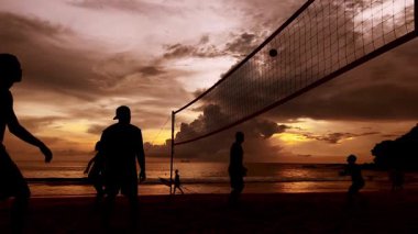Gençler gün batımında okyanus kenarında voleybol oynuyorlar..