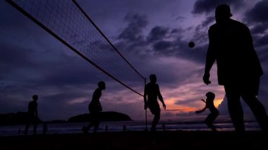 Gençler gün batımında okyanus kenarında voleybol oynuyorlar..