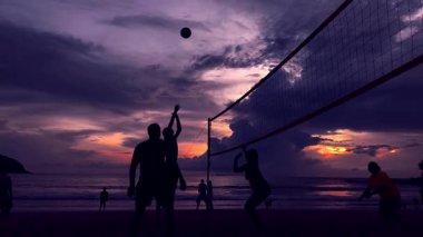 Gençler gün batımında okyanus kenarında voleybol oynuyorlar..