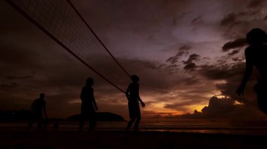 Gençler gün batımında okyanus kenarında voleybol oynuyorlar..
