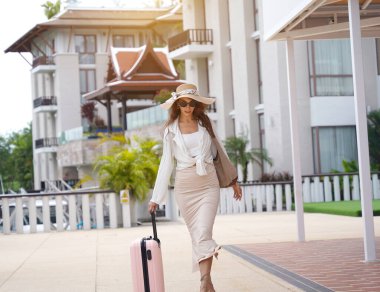 Bagajlı genç kadın yat limanının yanında yürüyor..