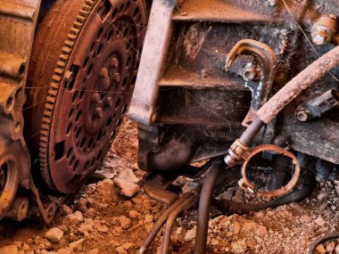 Paslanmış motor parçaları ve paslanmış dişliler kumlu zemine saçılmış..