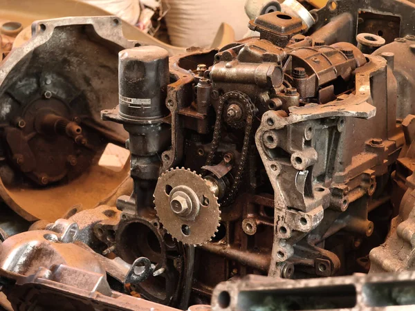 Paslanmış motor parçaları ve paslanmış dişliler kumlu zemine saçılmış..