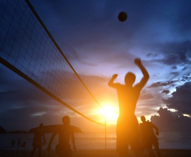 Gençler gün batımında okyanus kenarında voleybol oynuyorlar..