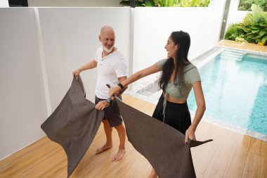 Bir erkek ve bir kadın kanepenin örtülerini birlikte sallıyor..