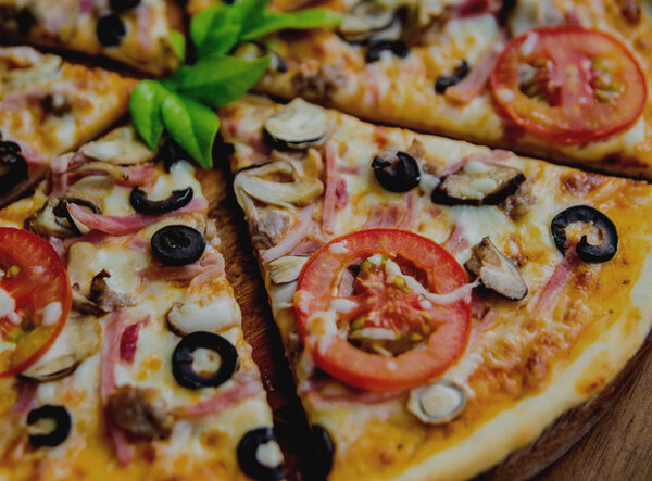 Large pizza with tomatoes and black olives on a wooden table