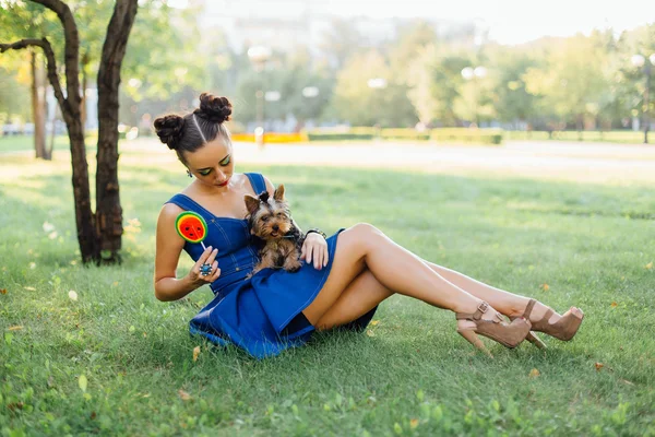 Maquiagem brilhante menina bonita com Yorkshire Terrier assentos na grama segurando pirulito melancia . — Fotografia de Stock