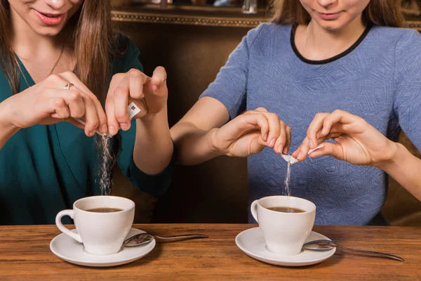 手中两个女人把糖放在一杯咖啡 — 图库照片
