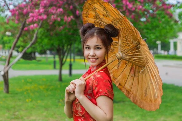 Schöne asiatische Mädchen in traditionellen chinesischen roten Kleid mit Bambusschirm. — Stockfoto