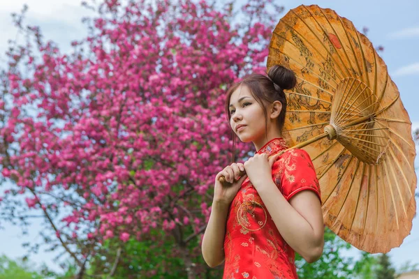 Schöne asiatische Mädchen in traditionellen chinesischen roten Kleid mit Bambusschirm. — Stockfoto