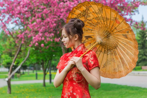 Vackra asiatiska flicka i traditionell kinesiska röda klänning med bambu paraply. — Stockfoto