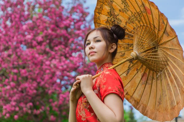 Schöne asiatische Mädchen in traditionellen chinesischen roten Kleid mit Bambusschirm. — Stockfoto