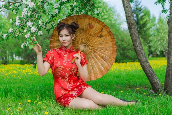 Schöne asiatische Mädchen in traditionellen chinesischen roten Kleid mit Bambusschirm. — Stockfoto