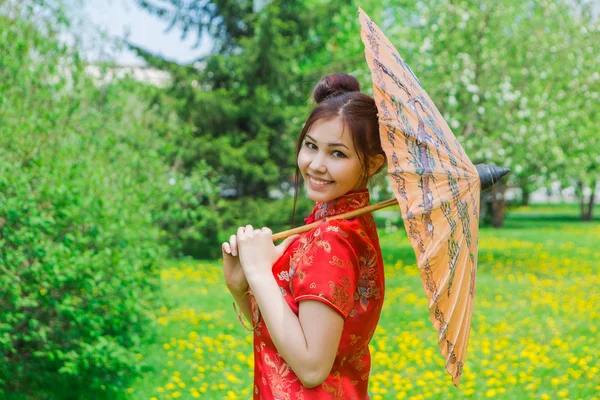 Beautiful asian girl in traditional chinese red dress with bamboo umbrella. — Stock Photo, Image