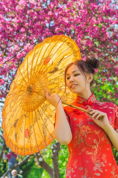 Beautiful asian girl in traditional chinese red dress with bamboo umbrella. — Stock Photo, Image