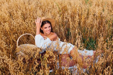 Kırsal Kır Sahnesi. Beyaz bluz ve hasır şapka giymiş, uzun saçlı genç ve güzel bir kadın altın yulaf tarlasında, yulaf kulaklı sepeti tutuyordu..