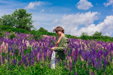 Yeşil ceketli uzun boylu yakışıklı bir adam lupin çiçeği tarlasında duruyor, doğanın güzelliğini emrediyor. Mor ve pembe lupinlerle çevrili bir adam..