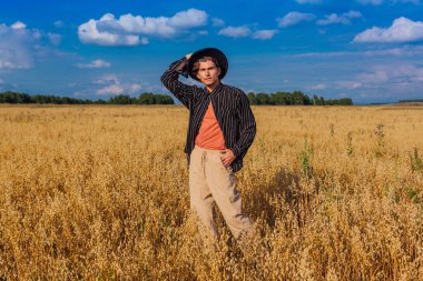 Kırsal Kır Sahnesi. Siyah gömlekli ve siyah şapkalı uzun boylu yakışıklı adam altın yulaf tarlasında duruyordu. Mavi gökyüzü ile yaz manzarası