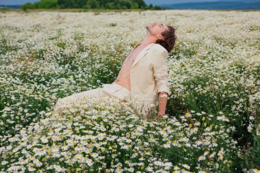 Beyaz takım elbiseli uzun boylu yakışıklı adam papatya çiçeği tarlasında beyaz bir sandalyede oturuyor.