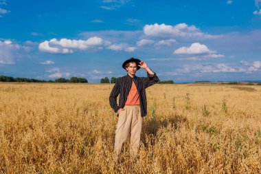 Kırsal Kır Sahnesi. Siyah gömlekli ve siyah şapkalı uzun boylu yakışıklı adam altın yulaf tarlasında duruyordu. Mavi gökyüzü ile yaz manzarası