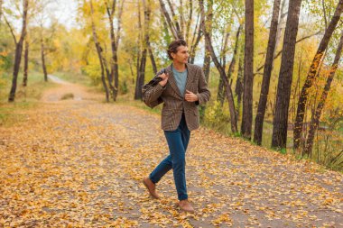 Kahverengi ceketli uzun boylu yakışıklı bir adam sonbahar sokağında çantasıyla yürüyor.