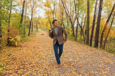 Kahverengi ceketli uzun boylu yakışıklı bir adam sonbahar sokağında çantasıyla yürüyor.