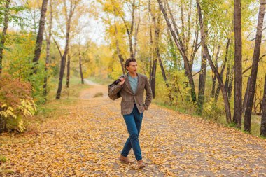 Kahverengi ceketli uzun boylu yakışıklı bir adam sonbahar sokağında çantasıyla yürüyor.