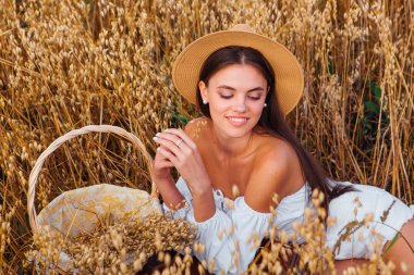 Kırsal Kır Sahnesi. Beyaz bluz ve hasır şapka giymiş, uzun saçlı genç ve güzel bir kadın altın yulaf tarlasında, yulaf kulaklı sepeti tutuyordu..