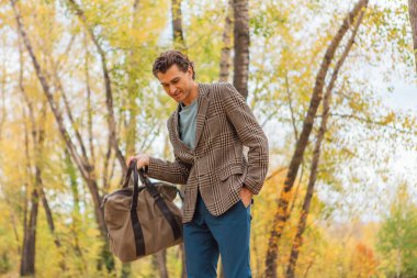 Kahverengi ceketli uzun boylu yakışıklı bir adam sonbahar sokağında çantasıyla yürüyor.