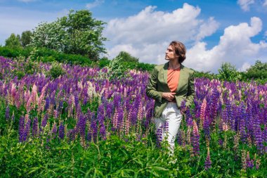 Yeşil ceketli uzun boylu yakışıklı bir adam lupin çiçeği tarlasında duruyor, doğanın güzelliğini emrediyor. Mor ve pembe lupinlerle çevrili bir adam..