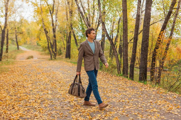 Kahverengi ceketli uzun boylu yakışıklı bir adam sonbahar sokağında çantasıyla yürüyor.
