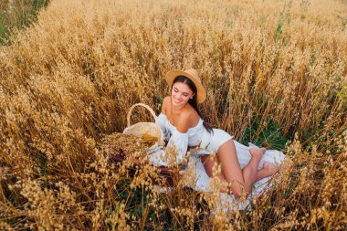 Kırsal Kır Sahnesi. Beyaz bluz ve hasır şapka giymiş, uzun saçlı genç ve güzel bir kadın altın yulaf tarlasında, yulaf kulaklı sepeti tutuyordu..