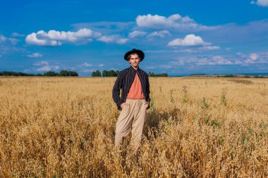 Kırsal Kır Sahnesi. Siyah gömlekli ve siyah şapkalı uzun boylu yakışıklı adam altın yulaf tarlasında duruyordu. Mavi gökyüzü ile yaz manzarası