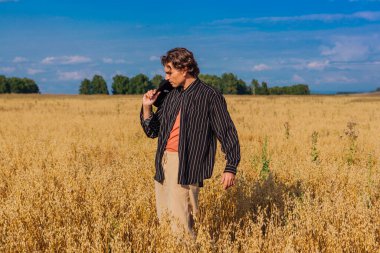 Kırsal Kır Sahnesi. Siyah gömlekli ve siyah şapkalı uzun boylu yakışıklı adam altın yulaf tarlasında duruyordu. Mavi gökyüzü ile yaz manzarası