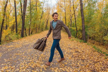 Kahverengi ceketli uzun boylu yakışıklı bir adam sonbahar sokağında çantasıyla yürüyor.