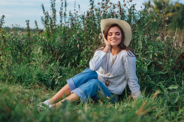 Νεαρή όμορφη μελαχρινή γυναίκα κάθεται στο γρασίδι και χαμογελώντας — Φωτογραφία Αρχείου