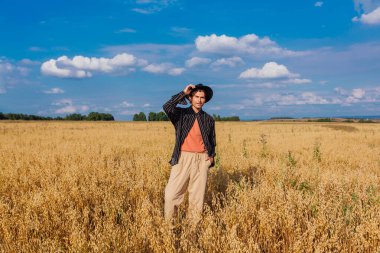 Altın yulaf tarlasında duran siyah şapkalı uzun boylu yakışıklı adam..