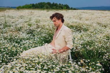 Papatya çiçeği tarlasında beyaz bir sandalyede oturan uzun boylu yakışıklı adam.