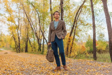 Sonbahar sokağında çantası olan uzun boylu yakışıklı bir adam.