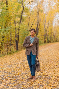 Sonbahar sokağında çantası olan uzun boylu yakışıklı bir adam.