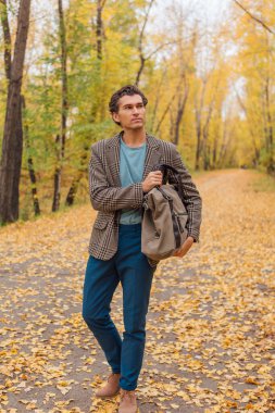 Kahverengi ceketli uzun boylu yakışıklı bir adam sonbahar sokağında çantasıyla yürüyor.